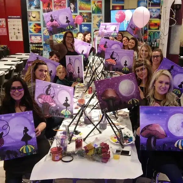 Group holding purple circus-themed paintings at a private event