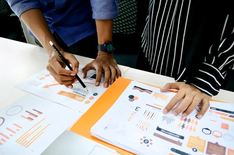 Hands analyzing marketing analytics documents with orange highlights