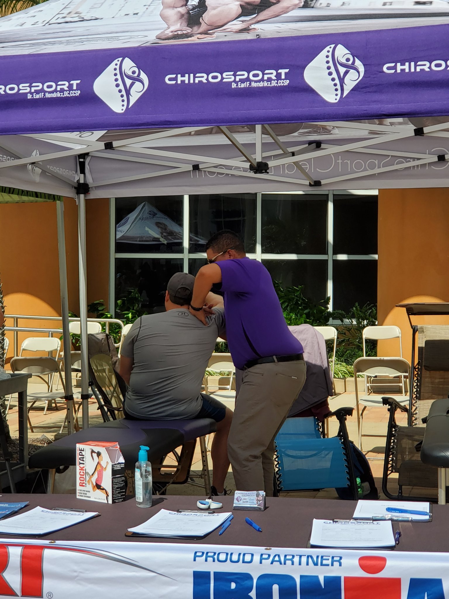 Dr. Hendrikz adjusting a seated athlete's shoulder and neck under the event treatment tent