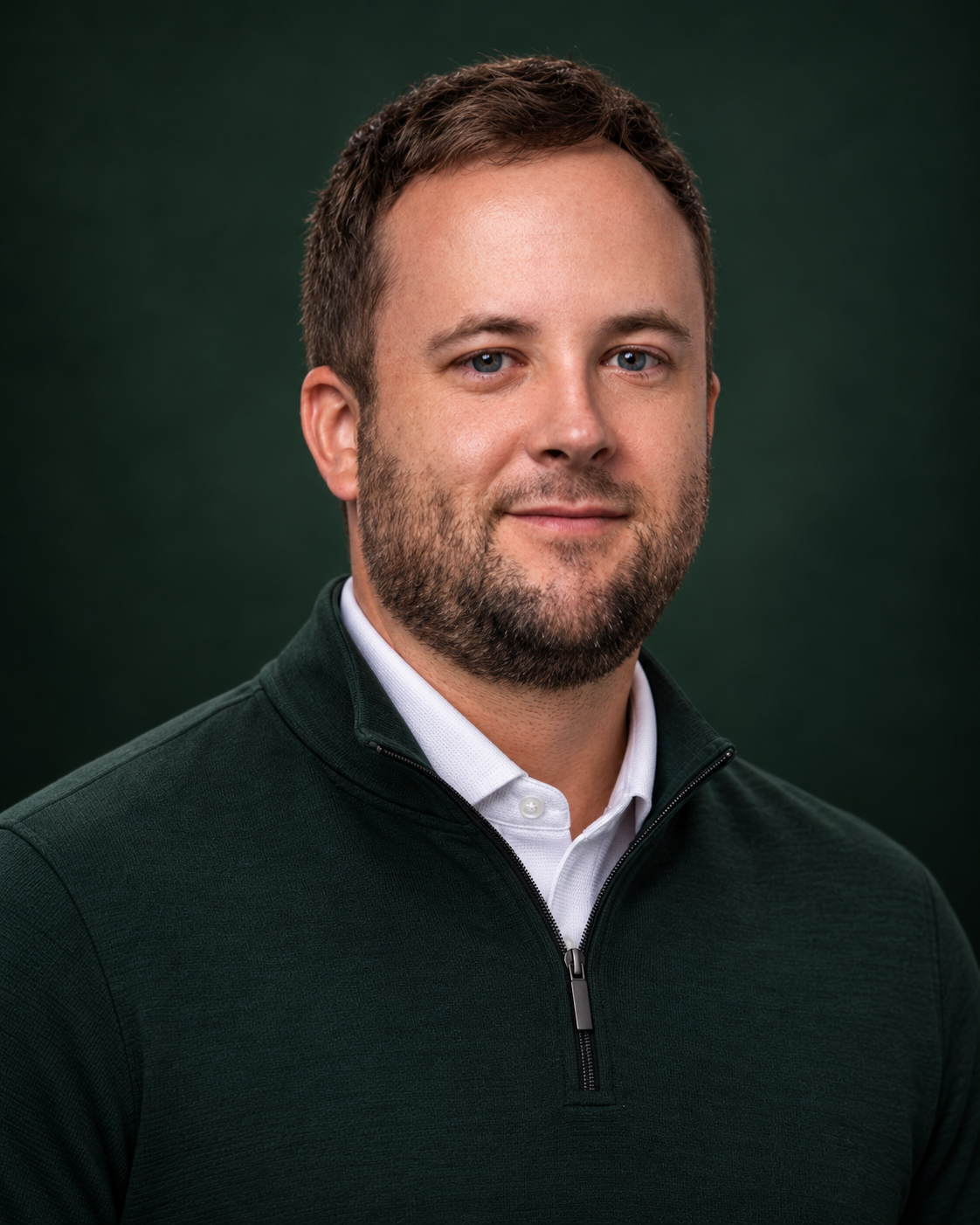 Man with short textured hair and a beard in a dark green quarter-zip