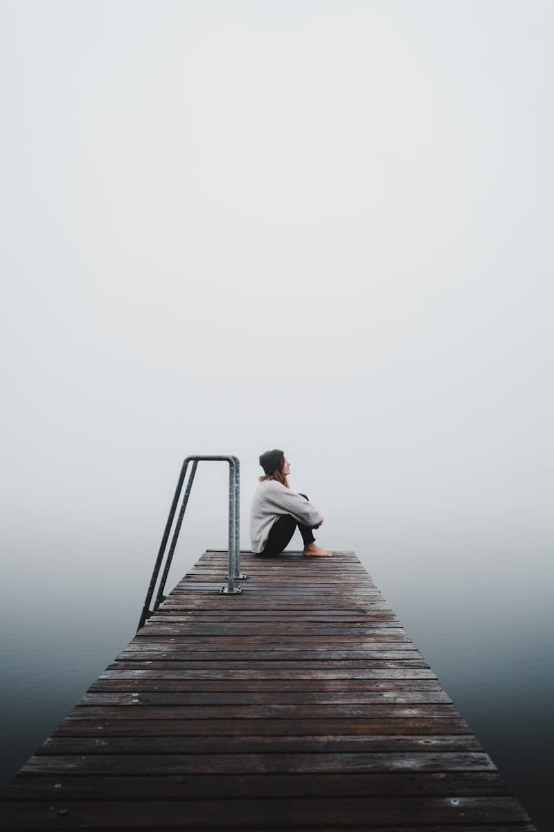 Pessoa sentada em um pier na neblina, em paz consigo mesma