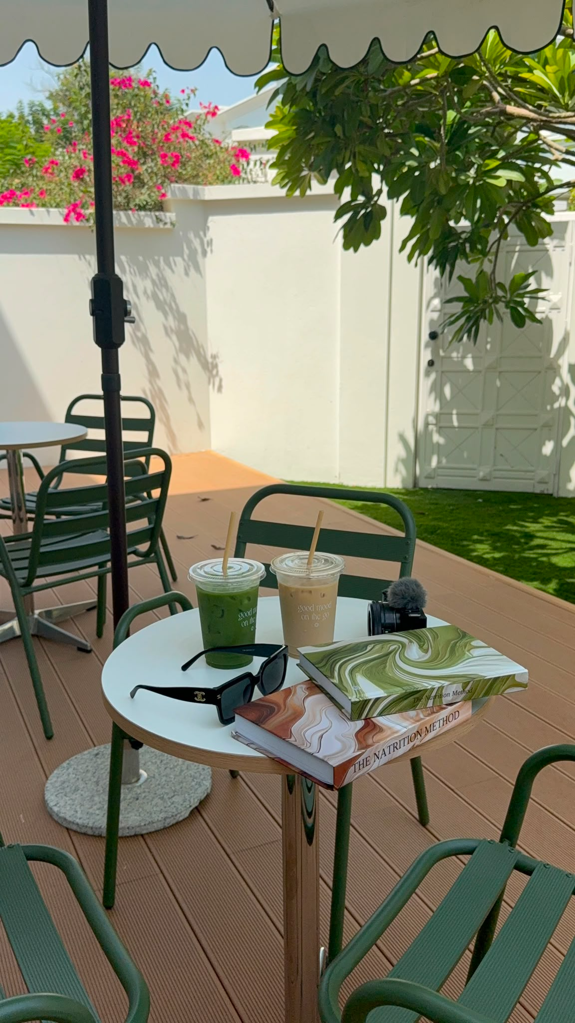 Both editions of The Natrition Method journal stacked on an outdoor café table with iced matcha, coffee and sunglasses