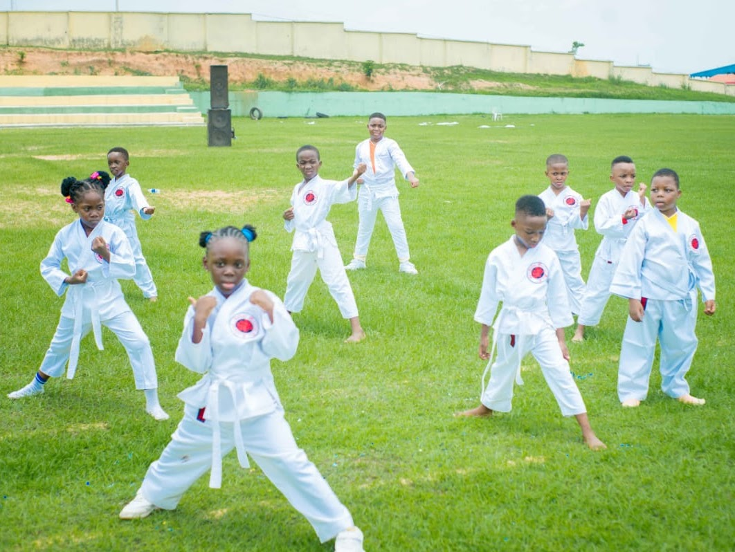 Children in martial-arts uniforms practicing on a grass field