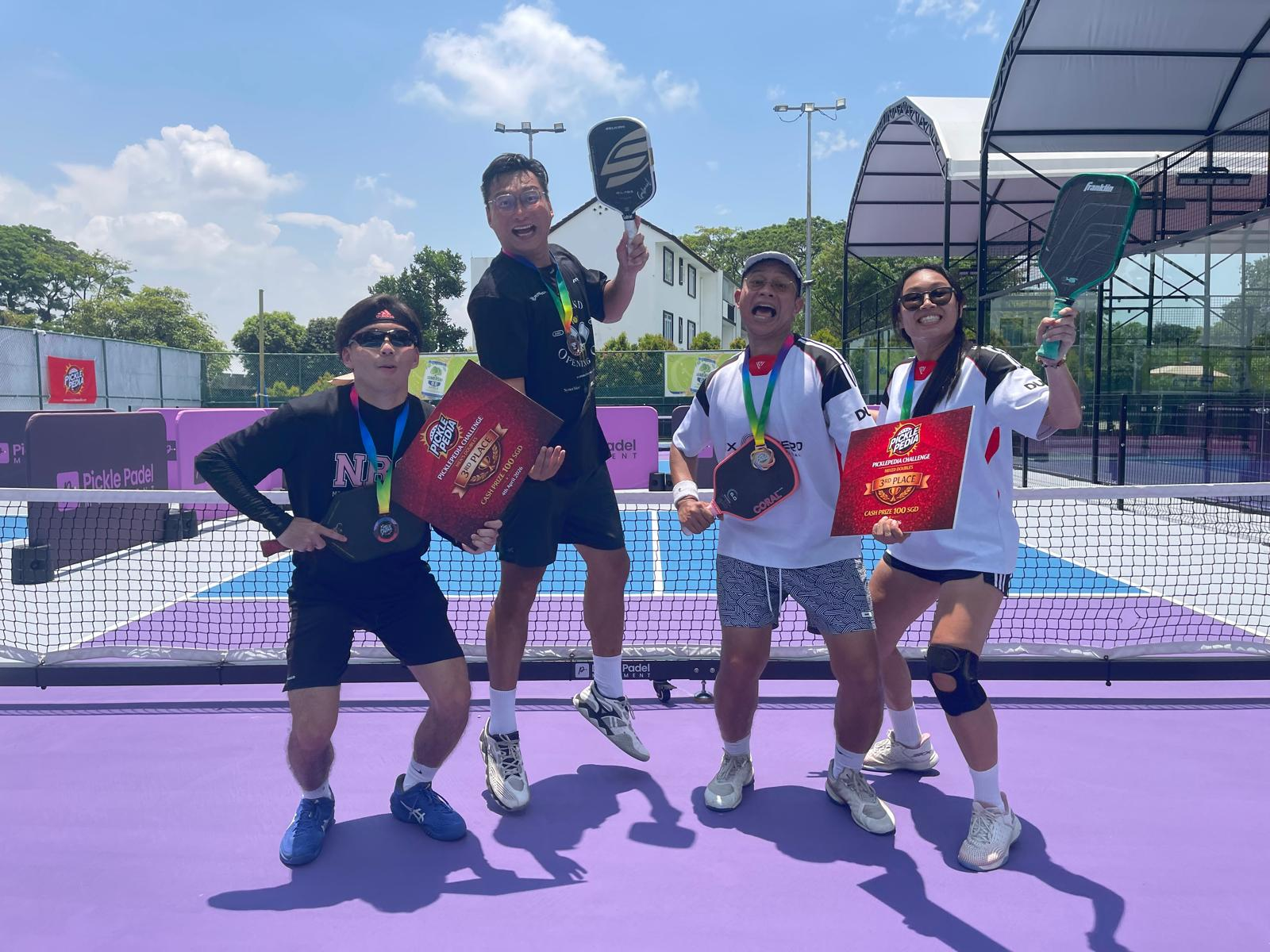 Third place winners celebrating with paddles and prize boards on purple court