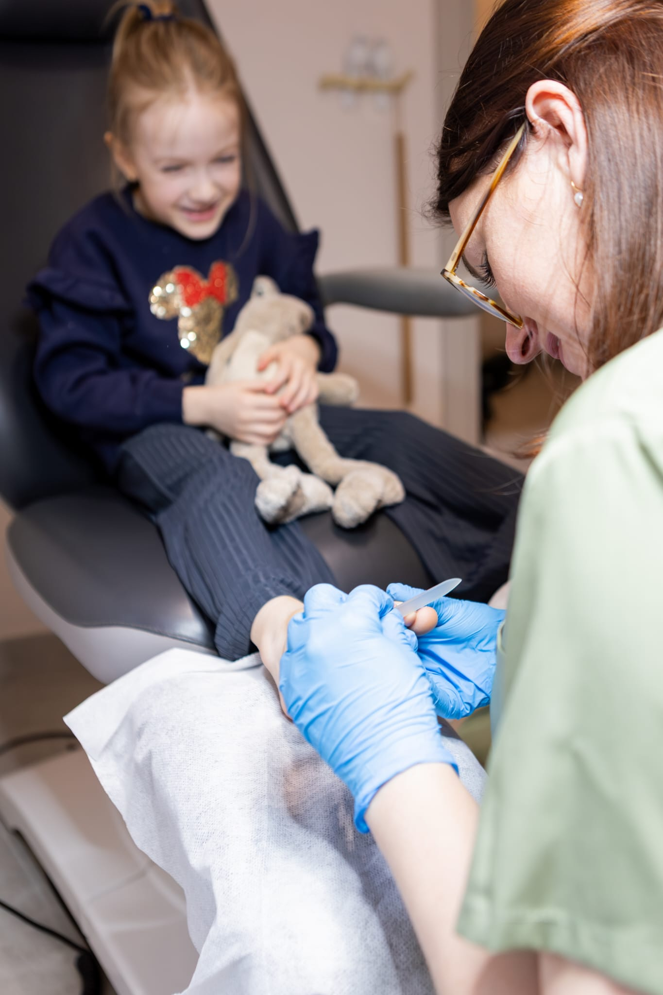 Karolina Szynwelska wykonująca zabieg podologiczny u małej dziewczynki trzymającej pluszaka