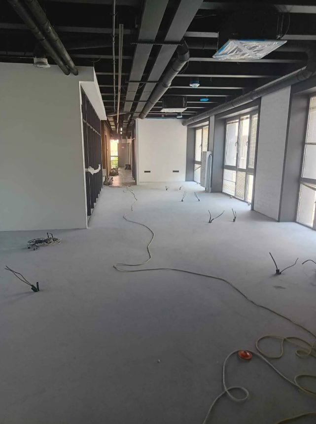 Large commercial space under construction showing exposed steel ceiling, HVAC ductwork, and open floor plan