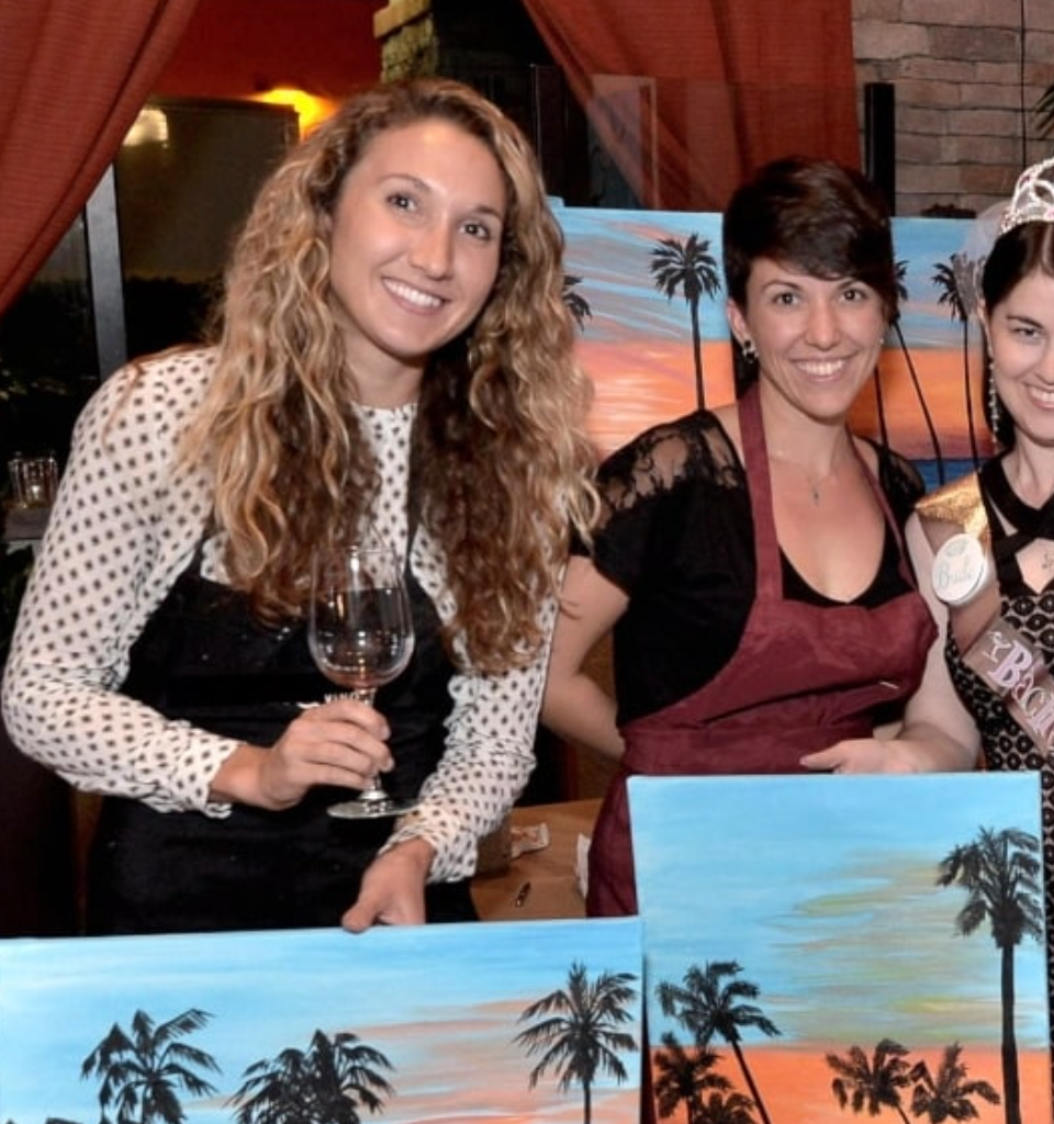 Bachelorette party group smiling with palm tree sunset paintings
