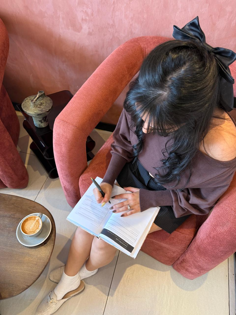 Overhead view of a woman journaling in a rust-colored armchair with a coffee on a side table
