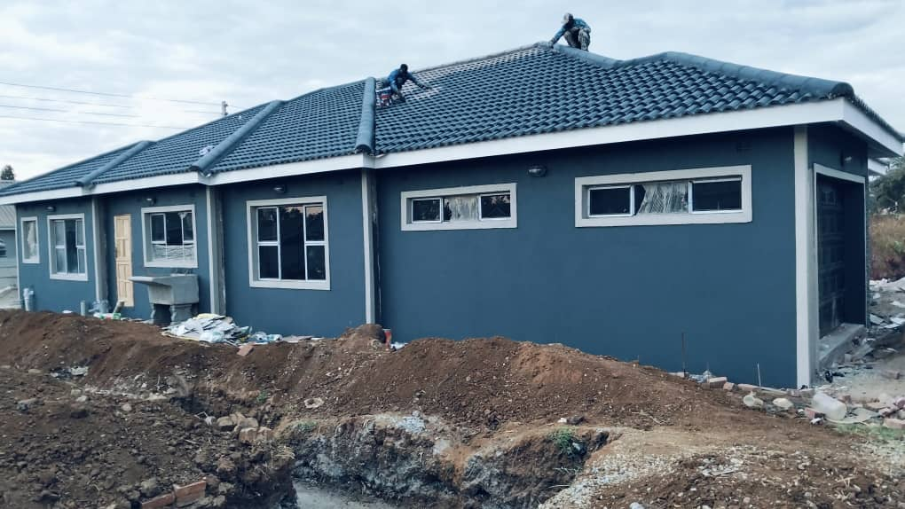 Workers laying roof tiles on a freshly painted blue house mid-construction