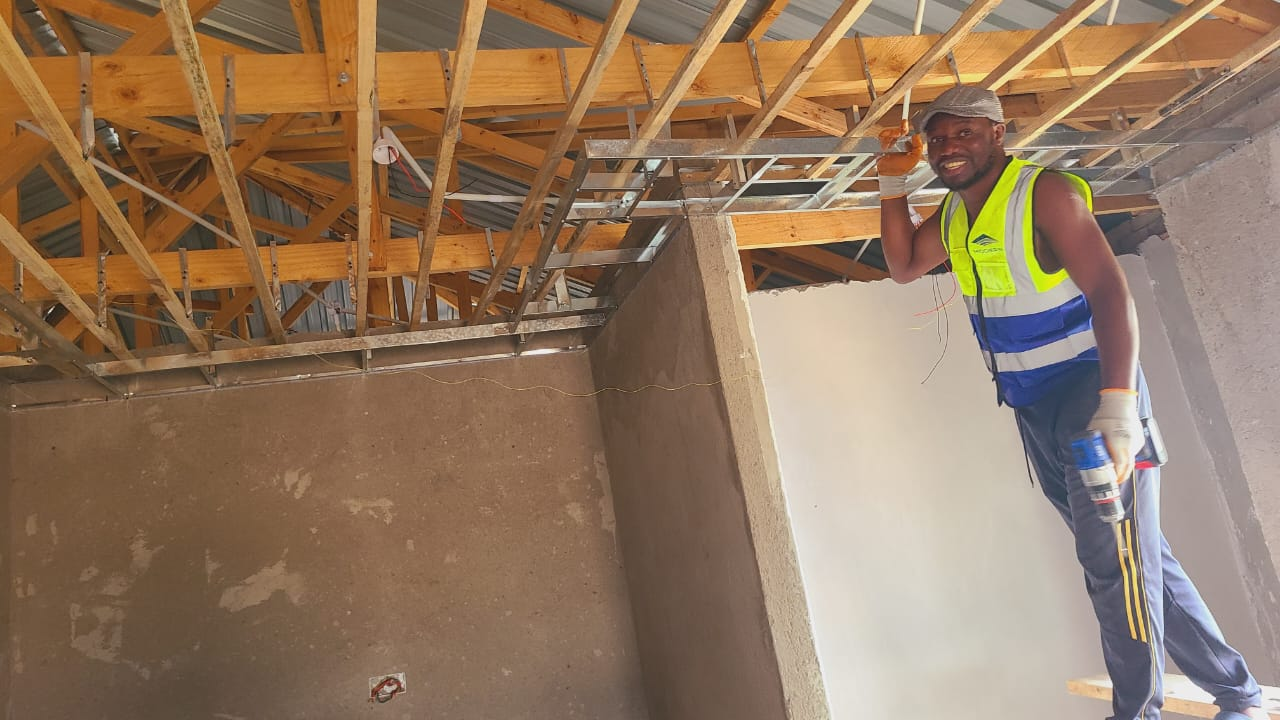 Team member installing metal ceiling framework with a drill on site