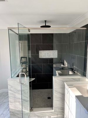 Large frameless glass shower with dark charcoal tile and white marble floor