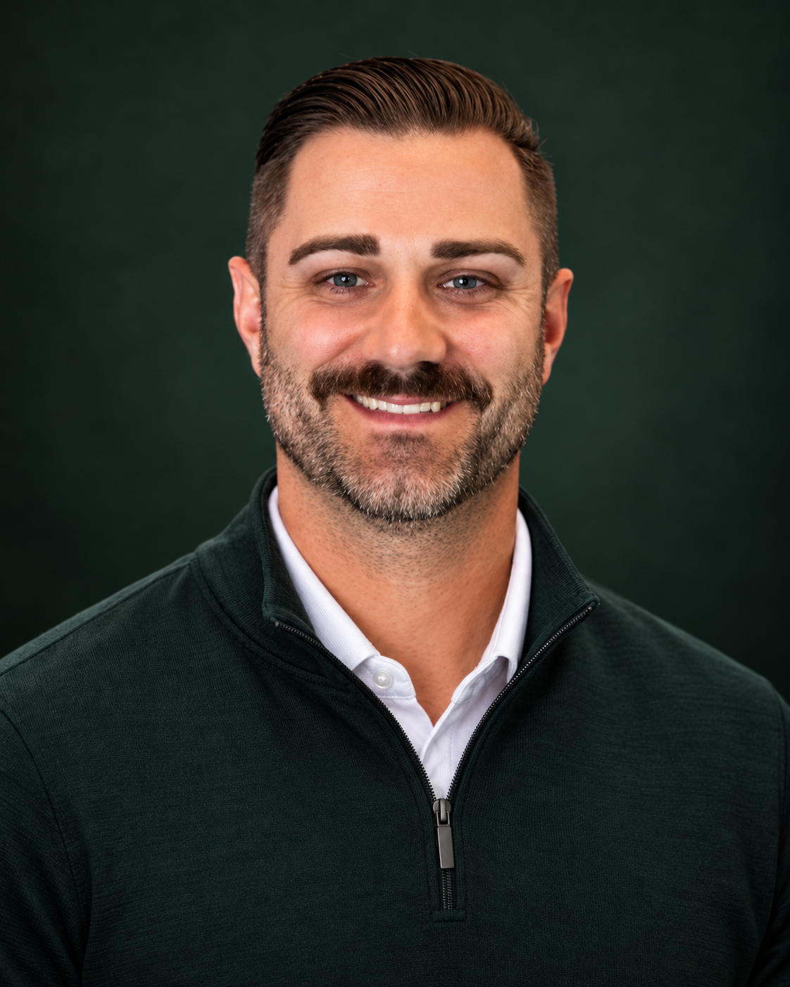 Smiling man with a mustache and neatly styled hair in a dark green quarter-zip