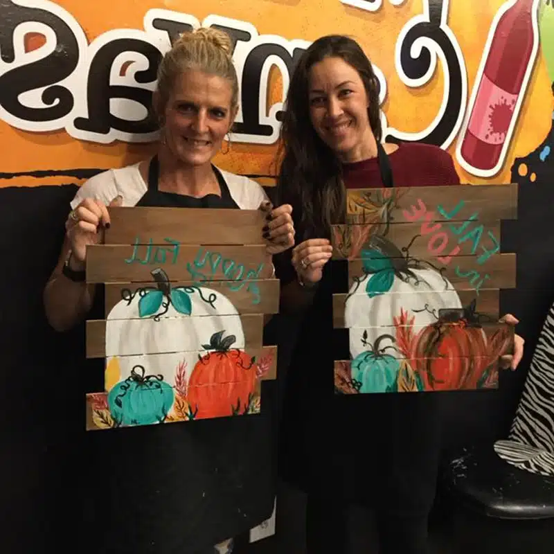 Two women holding painted pumpkin wood sign art