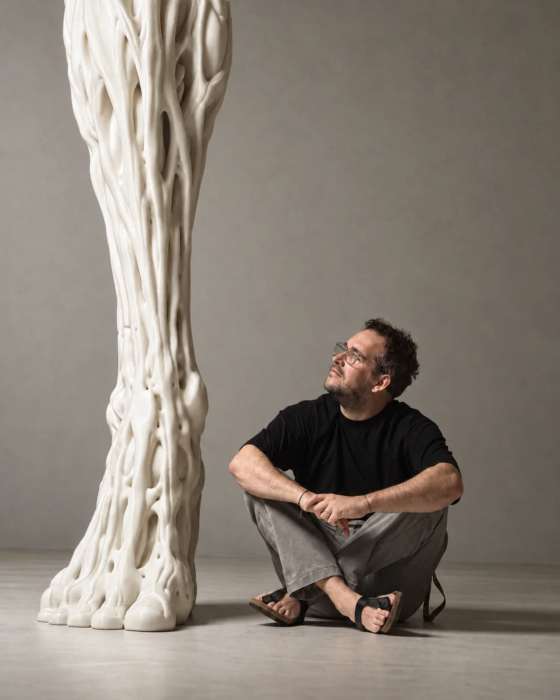Benjamin Rubi seated beside a tall, organically sculpted white artwork