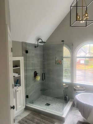 Frameless glass corner shower with gray tile, vaulted ceiling, and arched window