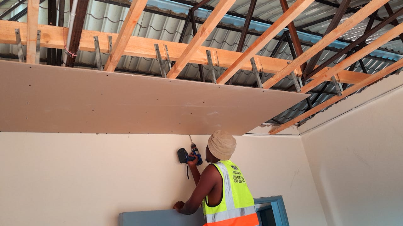 Worker drilling plasterboard into ceiling framework from below