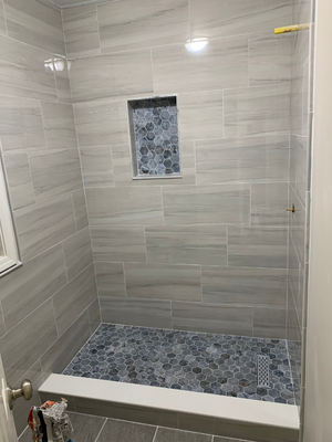 Shower with gray horizontal tile and blue hexagonal mosaic floor and niche