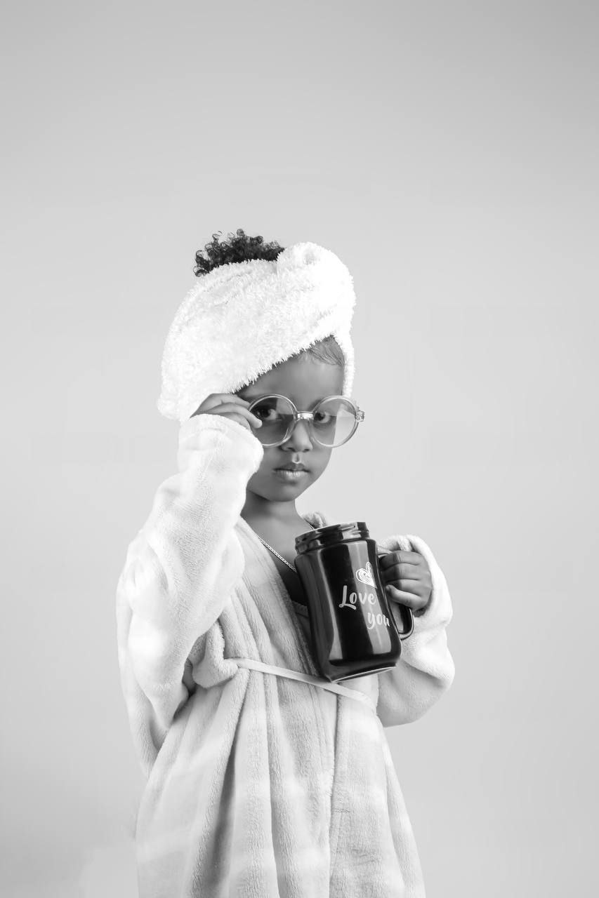 Child model in a white robe holding a black mug