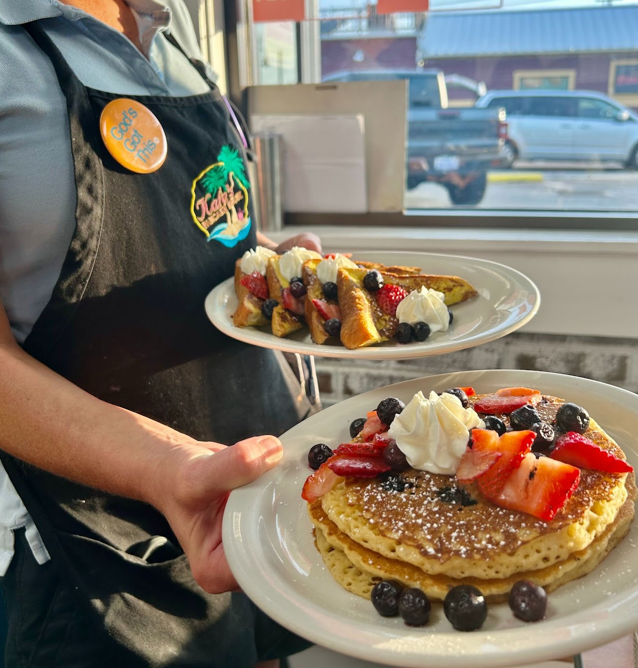 A server holding fruit-topped pancakes and French toast