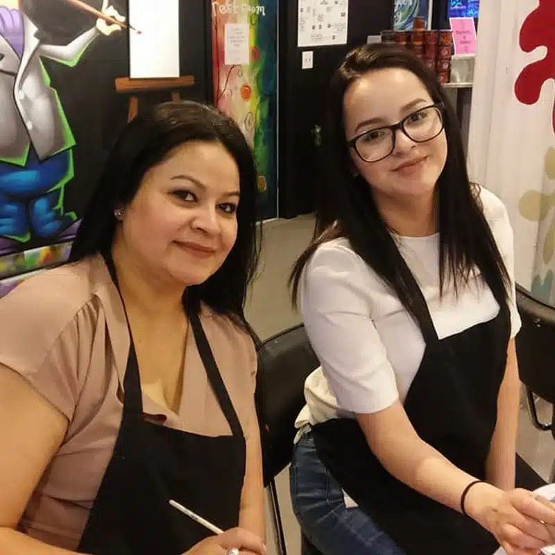 Two women smiling with aprons at a painting class
