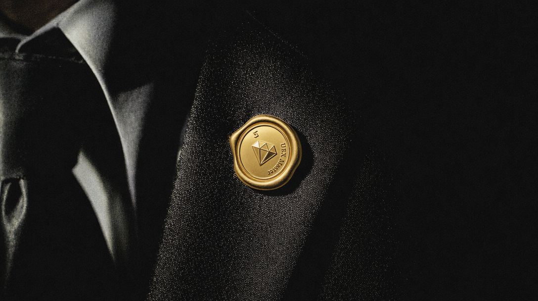 Bitget UEX Master — gold wax seal pin engraved with diamond icon on a dark satin suit lapel