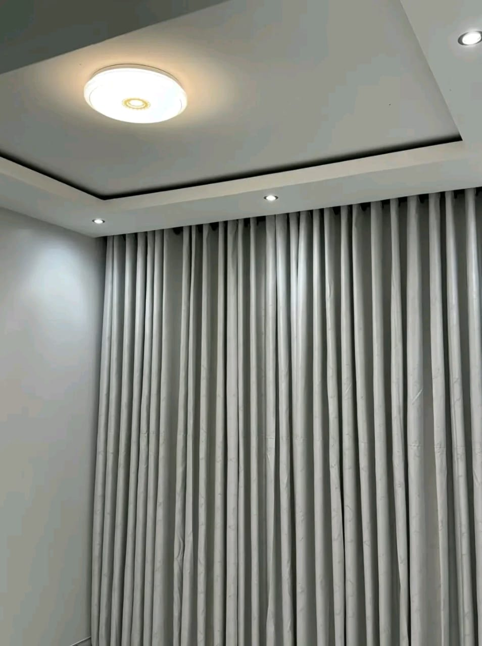 Stepped tray ceiling with round flush light and grey curtains