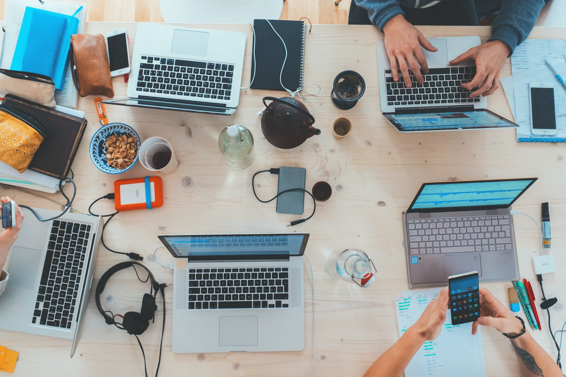 A bird's-eye view of a workspace with multiple laptops, devices, and office supplies on a wooden table