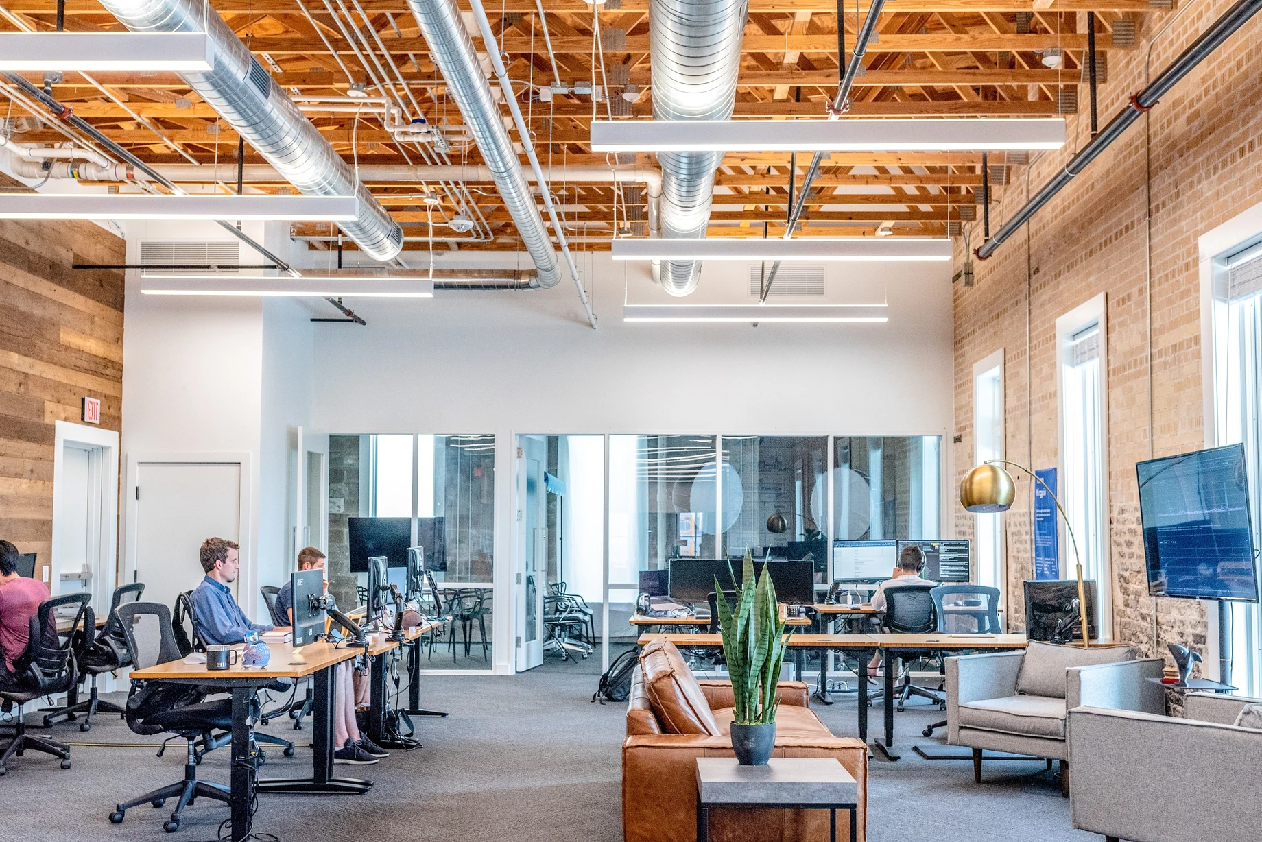 An open-plan office with exposed ceiling, modern furniture, and people working at desks