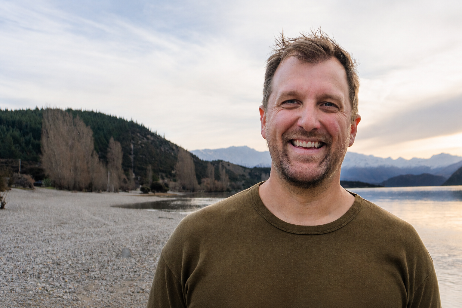 Portrait of Amos Breyfogle, Principal for Advanced Manufacturing and Strategy at Pivot Innovation, standing on a Queenstown lakeshore with snow-capped mountains behind