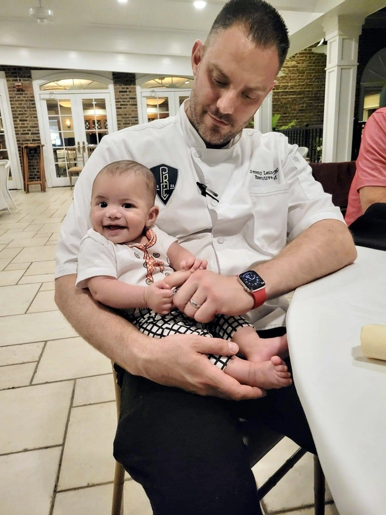 Jeremy Leinen in chef whites holding a smiling baby