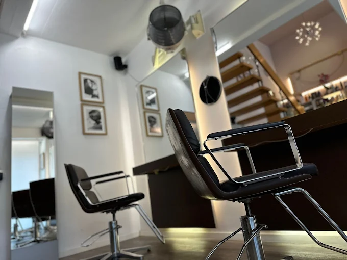 Salon E — Styling-Bereich mit schwarzen Designstühlen und Kunstdrucken