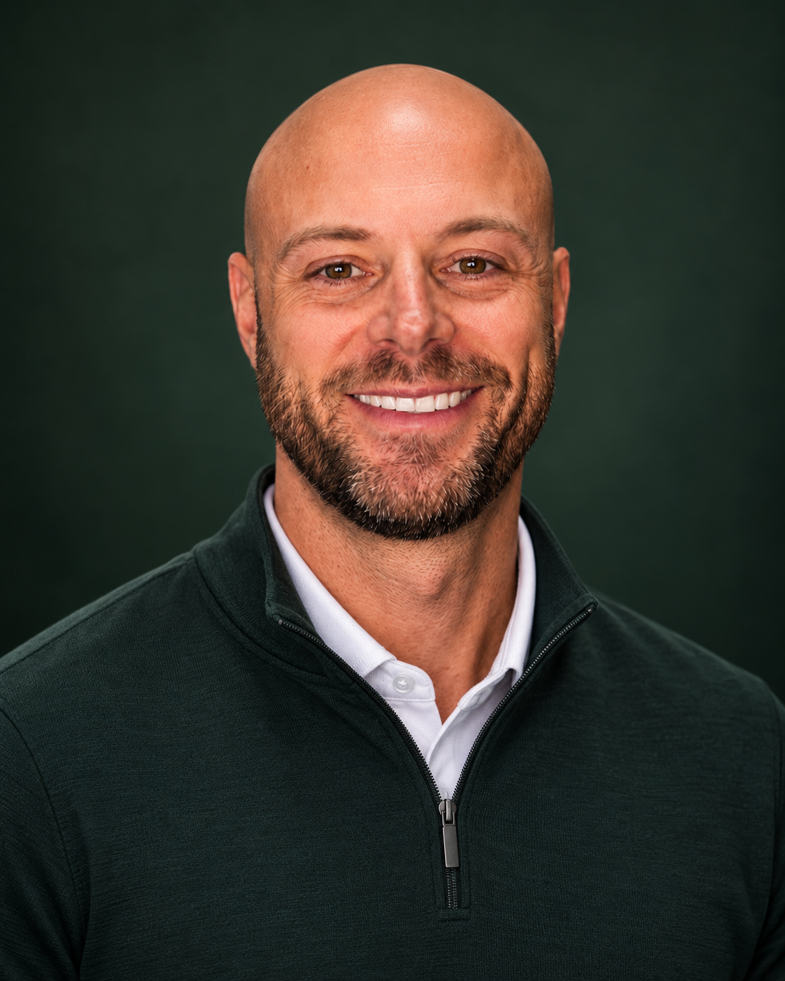 Smiling bald man with a beard in a dark green quarter-zip