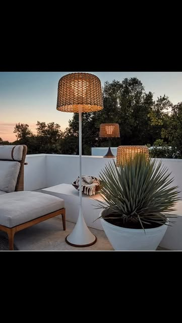 Sophisticated outdoor terrace at dusk with woven rattan floor lamps, beige lounge chair, white pedestal table, and tropical plant — outdoor living by Jayne Michelle Interiors
