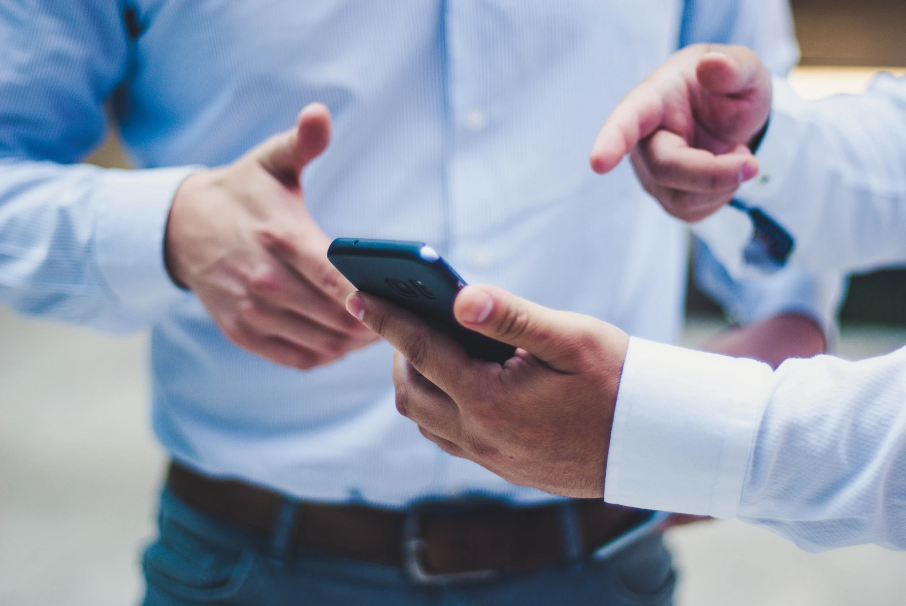 A close-up of two people's hands, one holding a smartphone and the other gesturing towards it