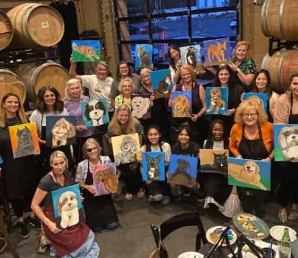 Large group of women in a winery holding pet portrait paintings