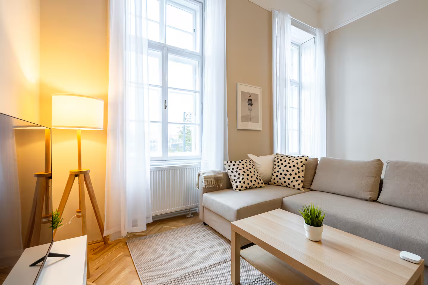 Bright living room with beige sofa, polka dot pillows, TV, and tall windows overlooking the city