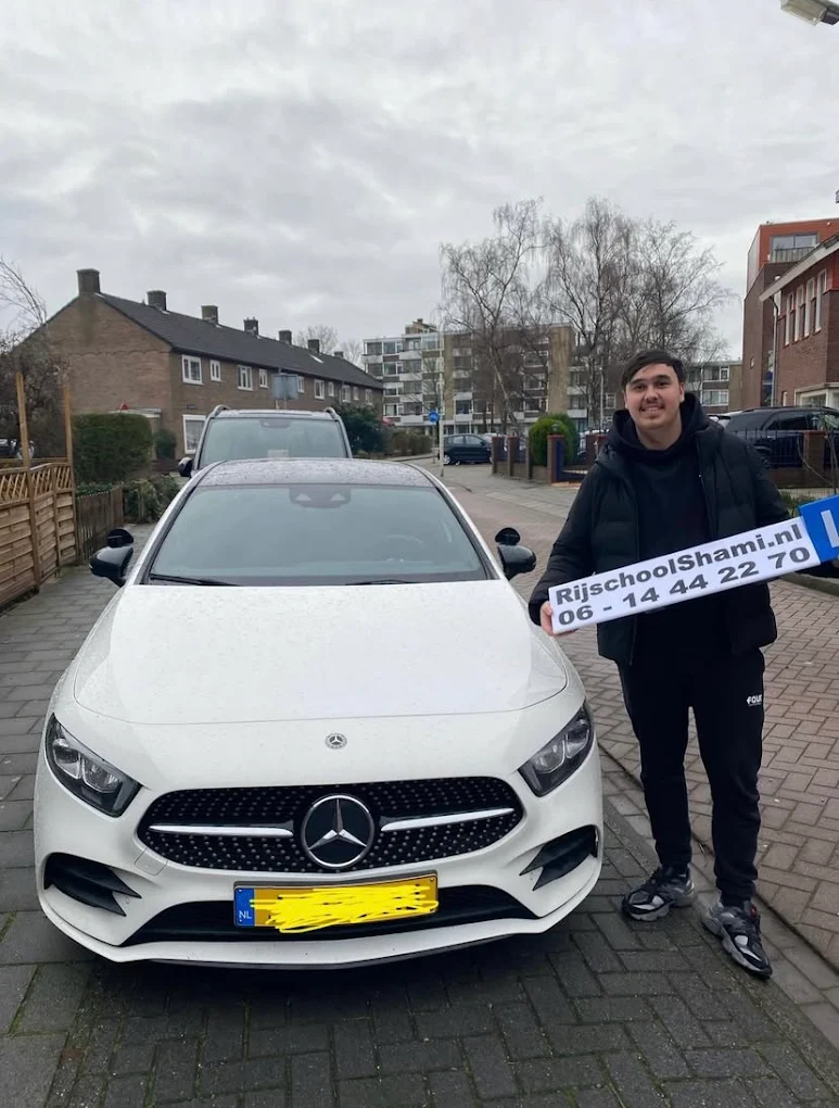 Geslaagde leerling met RijschoolShami.nl bord bij witte Mercedes