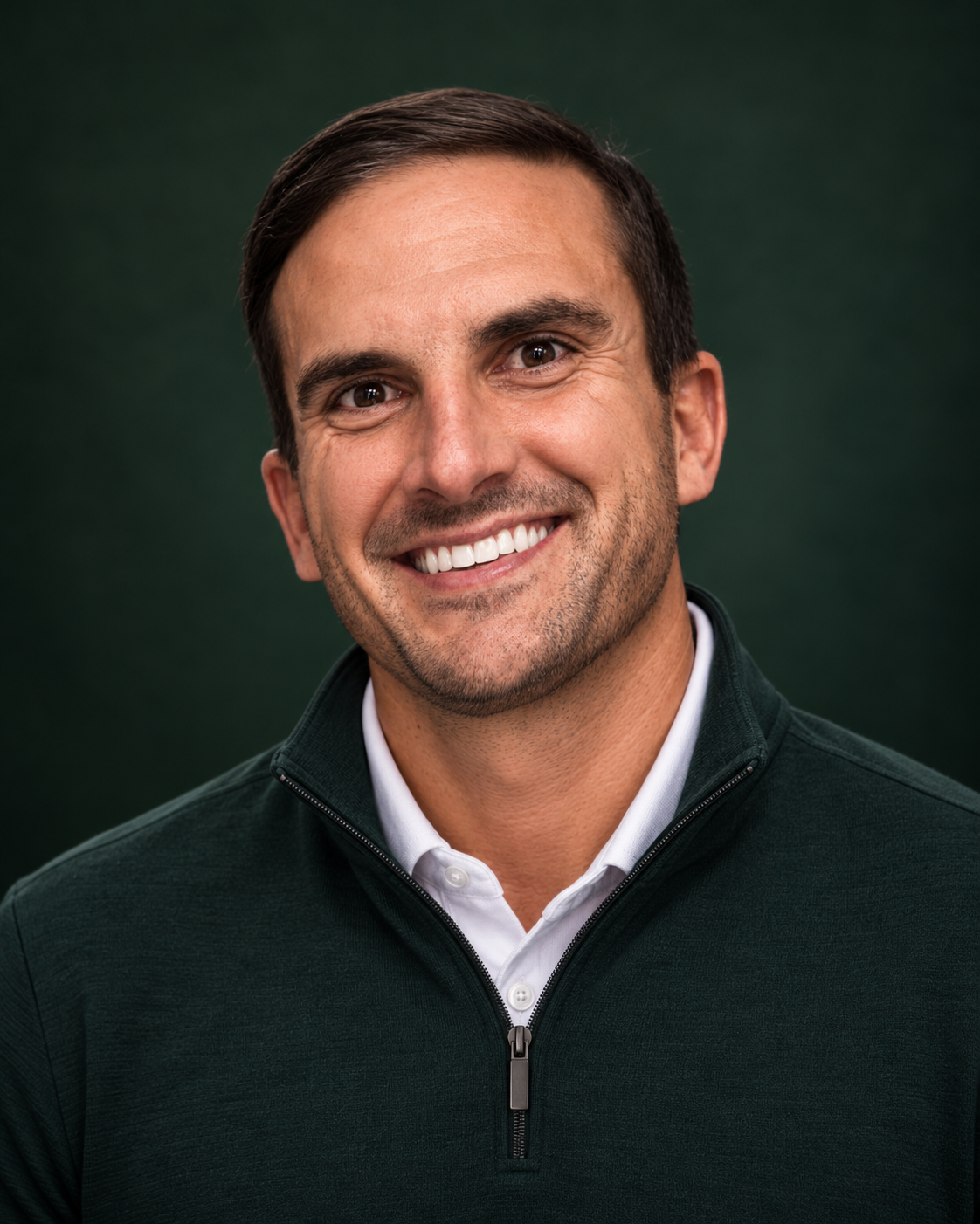 Smiling man with short dark hair and light stubble in a dark green quarter-zip