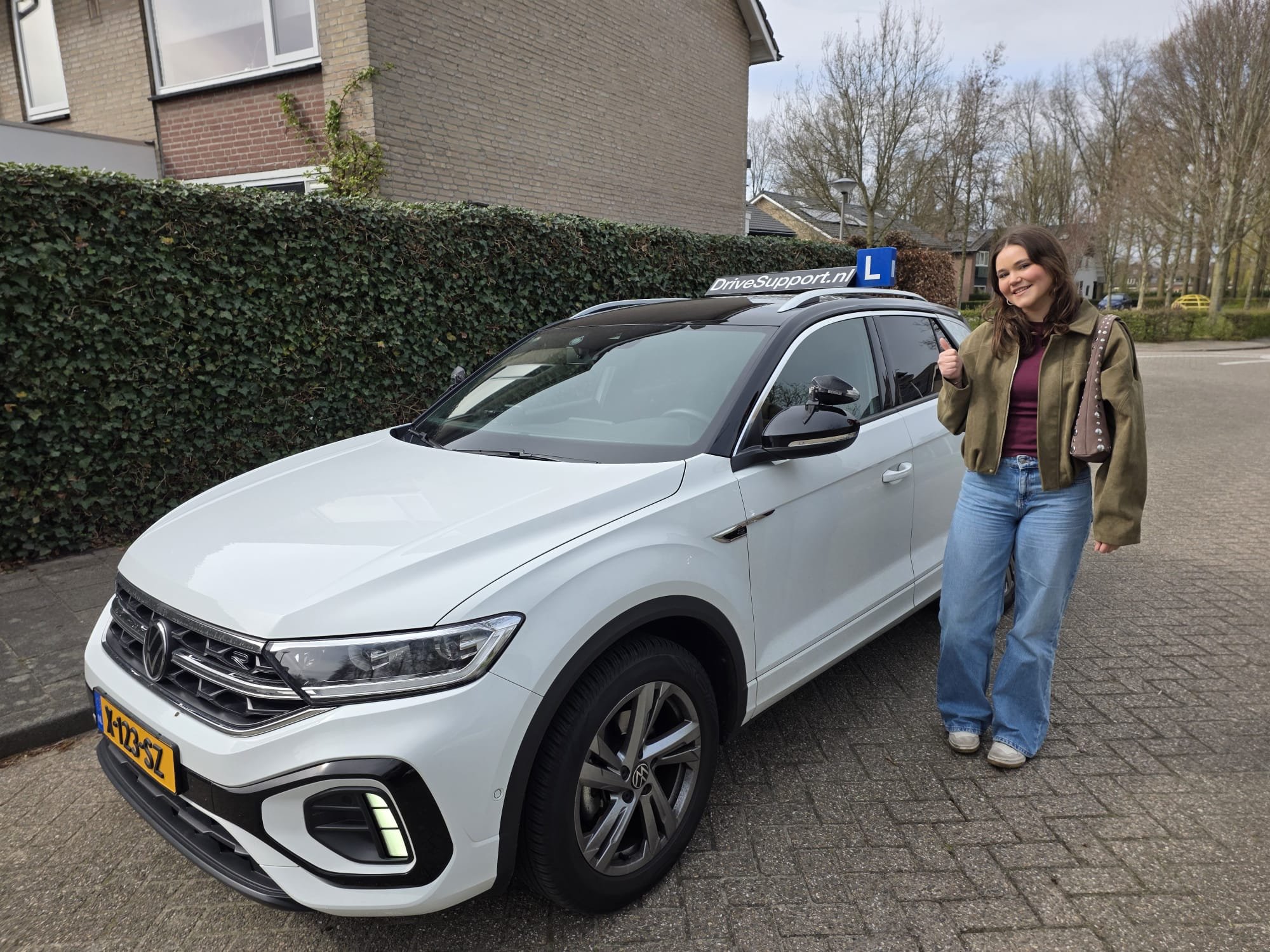 Leerling geeft duim omhoog naast de witte DriveSupport lesauto