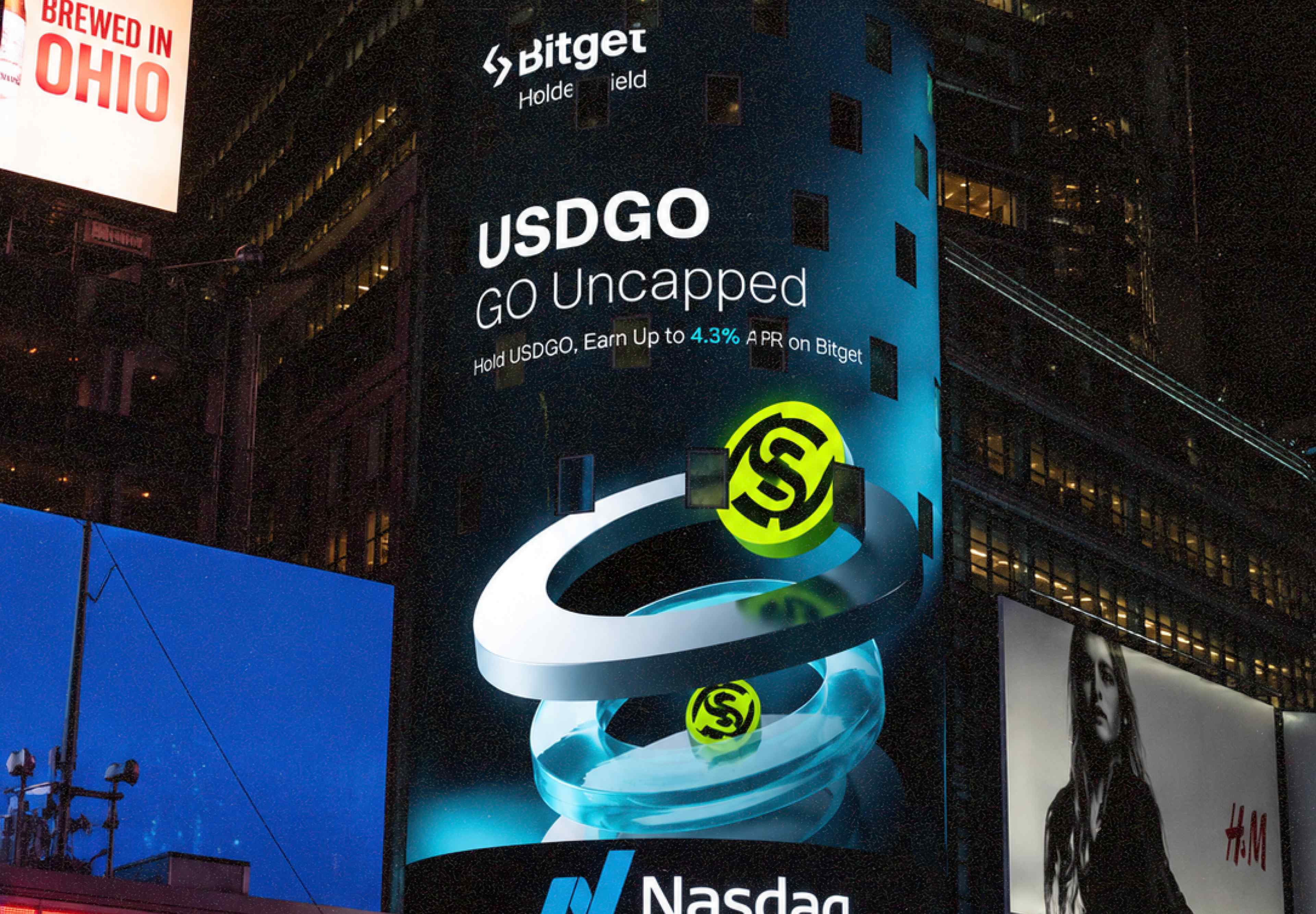 USDGO GO Uncapped — Bitget HolderYield on a massive curved building LED billboard in Times Square at night, Nasdaq logo at bottom