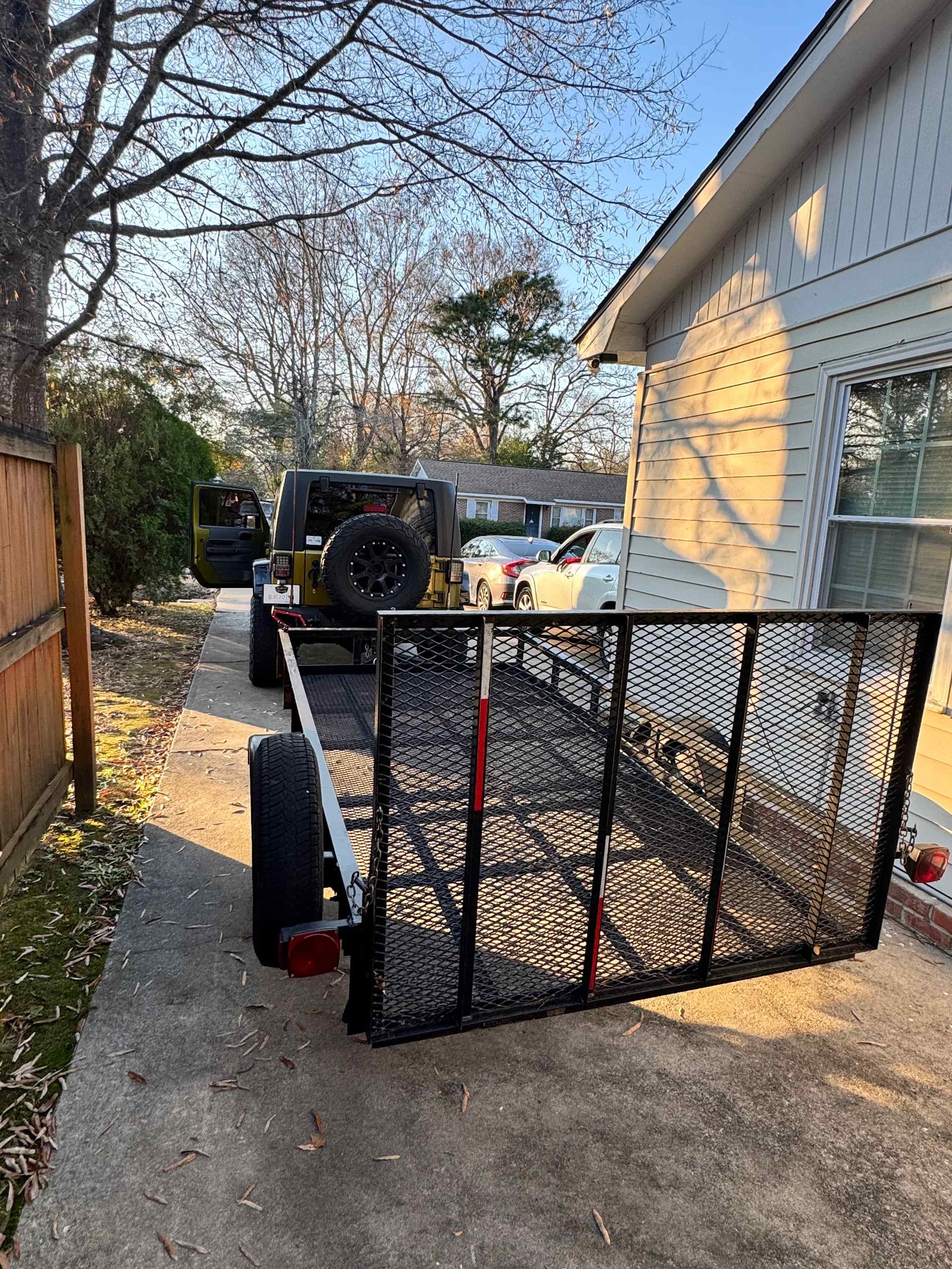 Utility trailer with mesh ramp gate hitched to a Jeep in a driveway
