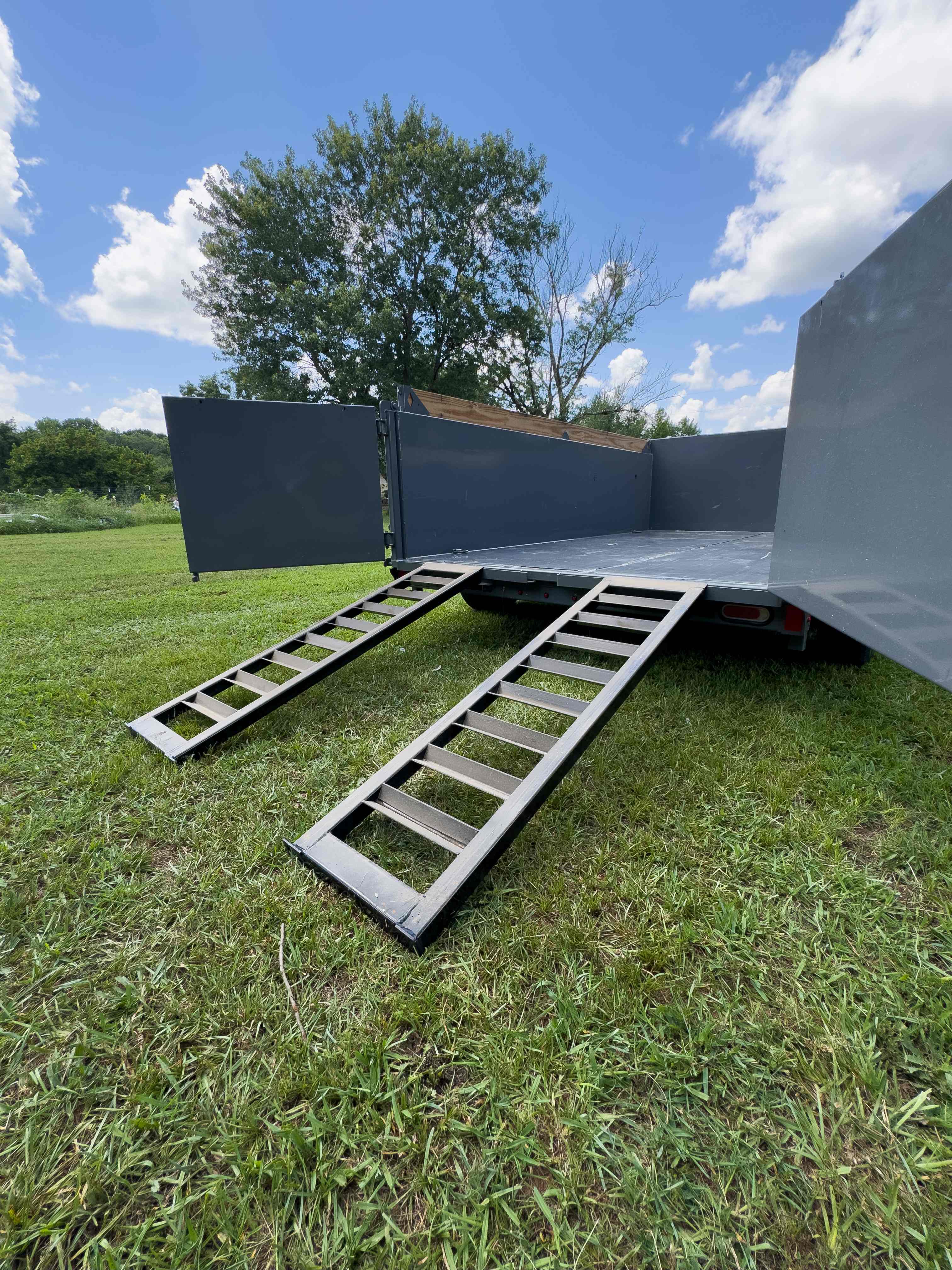 Dumpster trailer rear with barn doors open and loading ramps deployed on grass