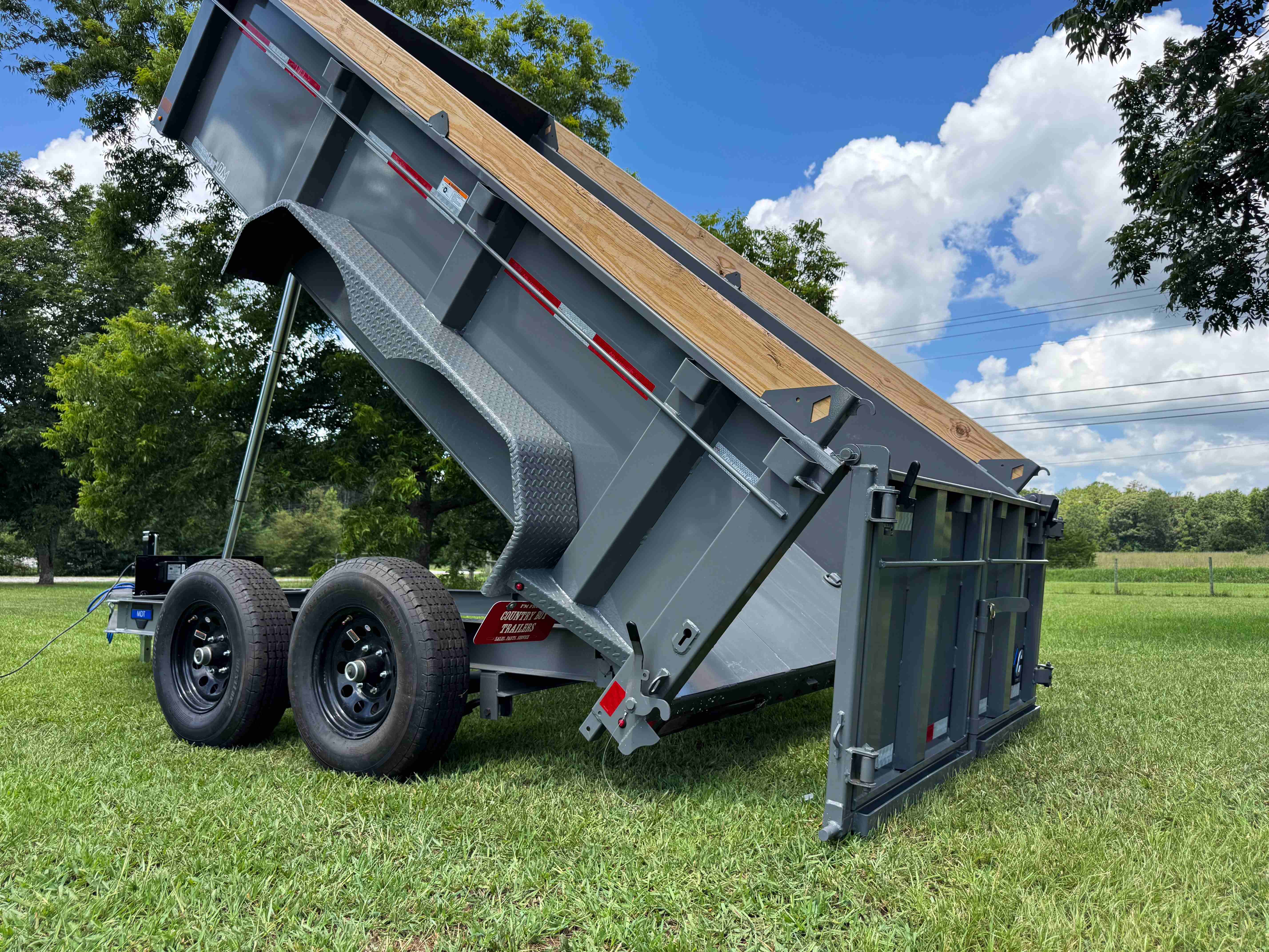 Dumpster trailer hydraulic dump raised at steep angle showing rear barn doors open