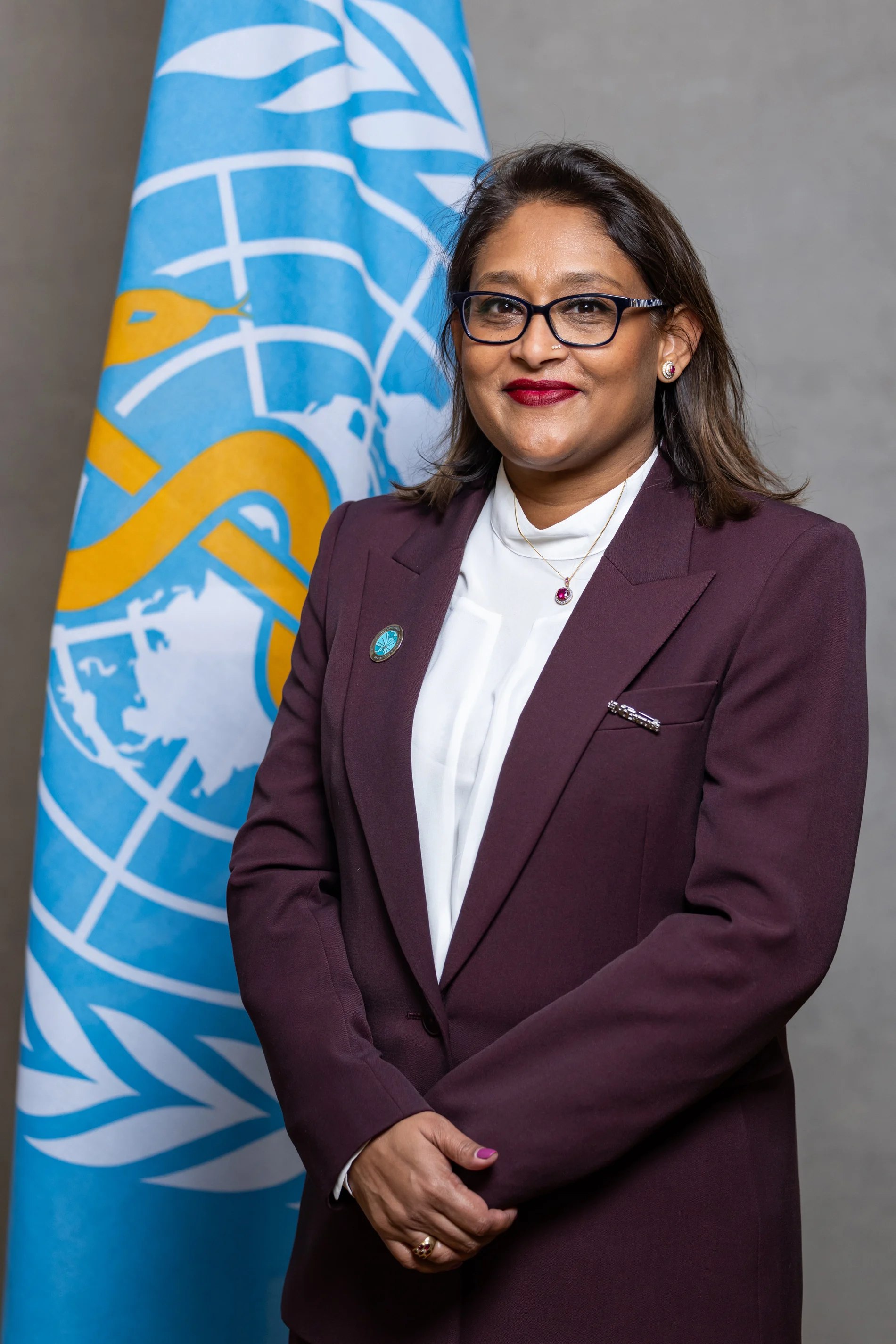 Formal portrait of Saima Wazed beside an international emblem flag