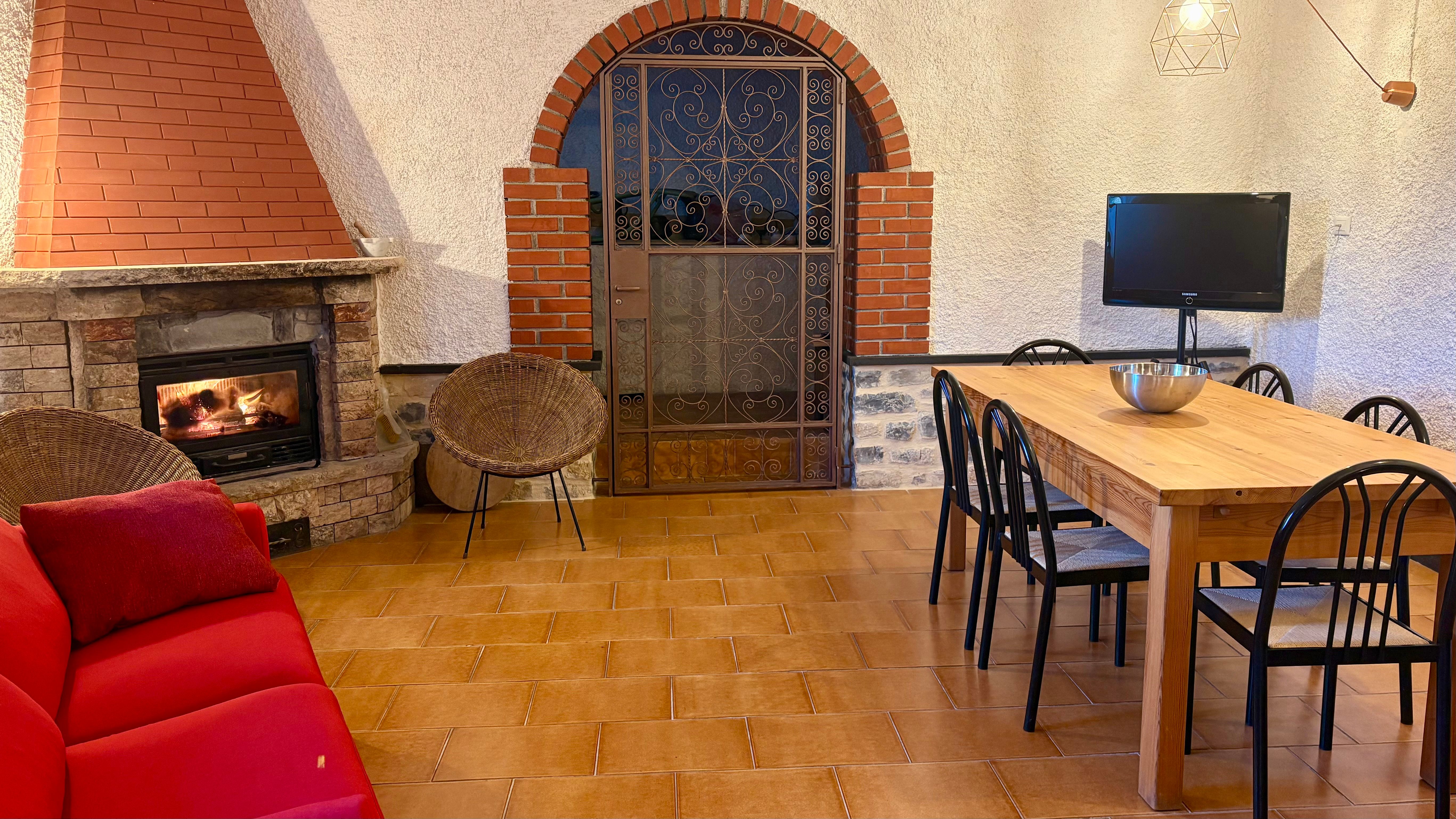 Salotto Ca Piera camino acceso divano rosso tavolo legno Diano Borello casa vacanze