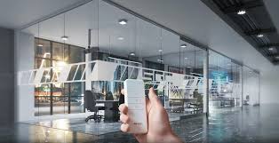 Hand holding a remote control pointing at smart glass partitions in a modern open office