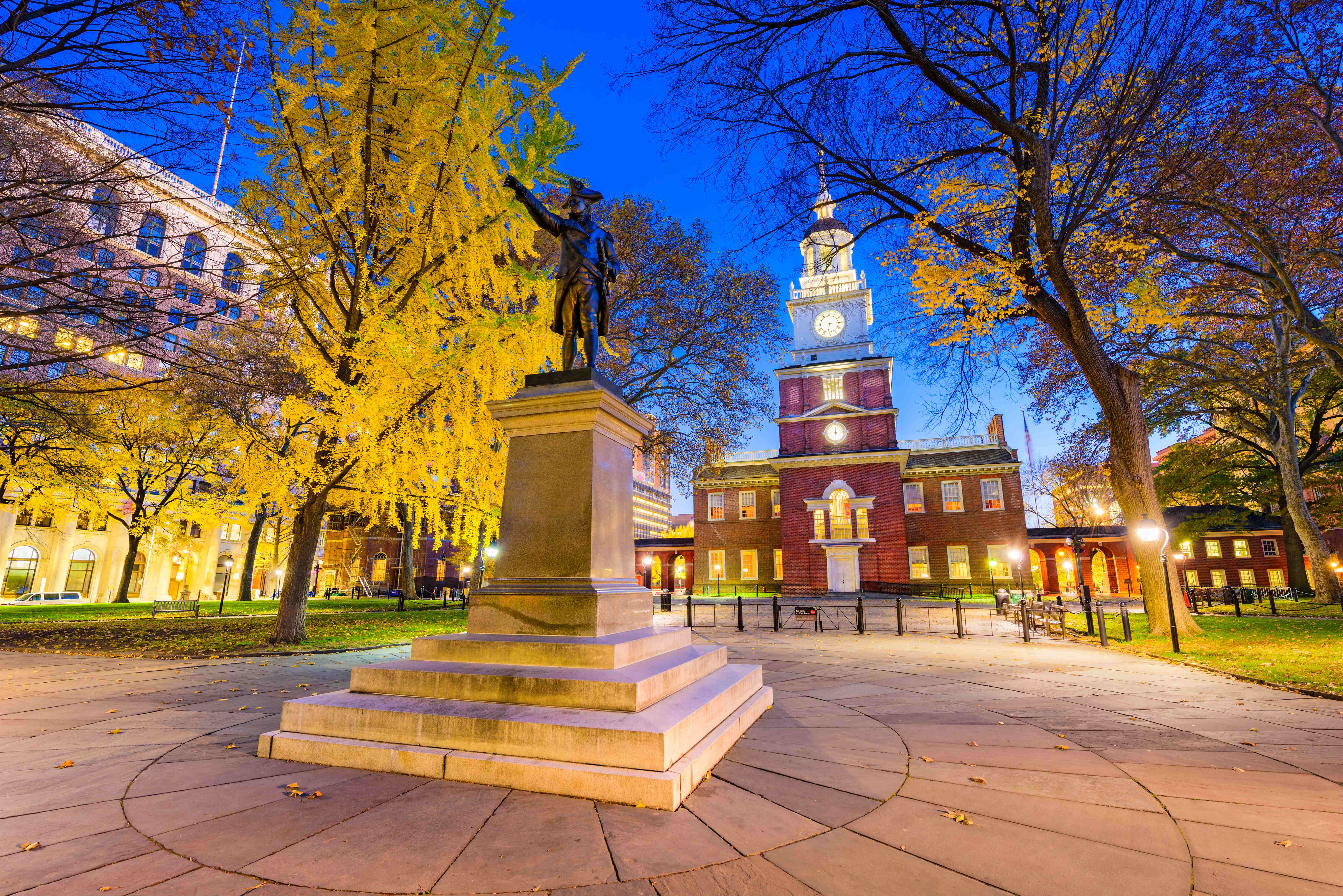 Independence Hall in Philadelphia lit at dusk with a statue in the foreground