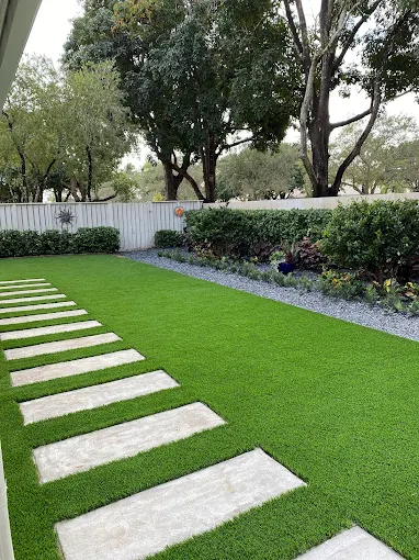 Artificial turf backyard installation with white stone stepping-stone pathway and manicured hedges