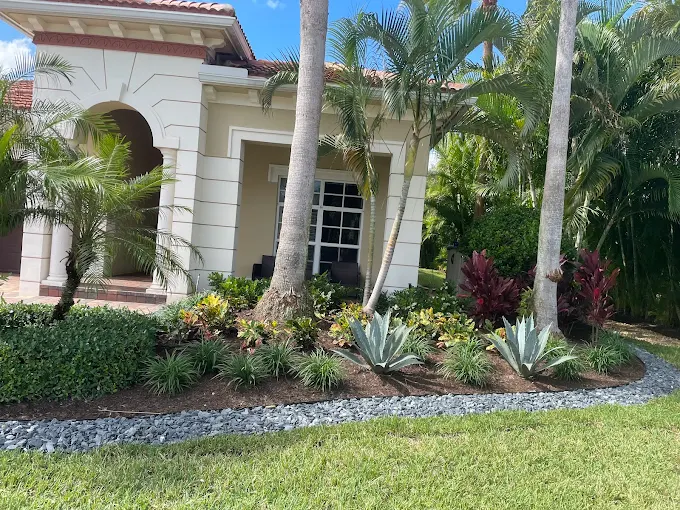 Completed tropical landscape installation at a luxury Palm Beach County home featuring agave, bromeliad, palms, and river rock border