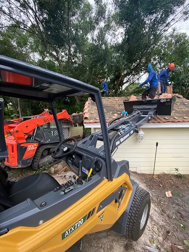 Integrity Landscape crew members clearing heavy storm debris from a residential roof with a skid steer and utility vehicle on site
